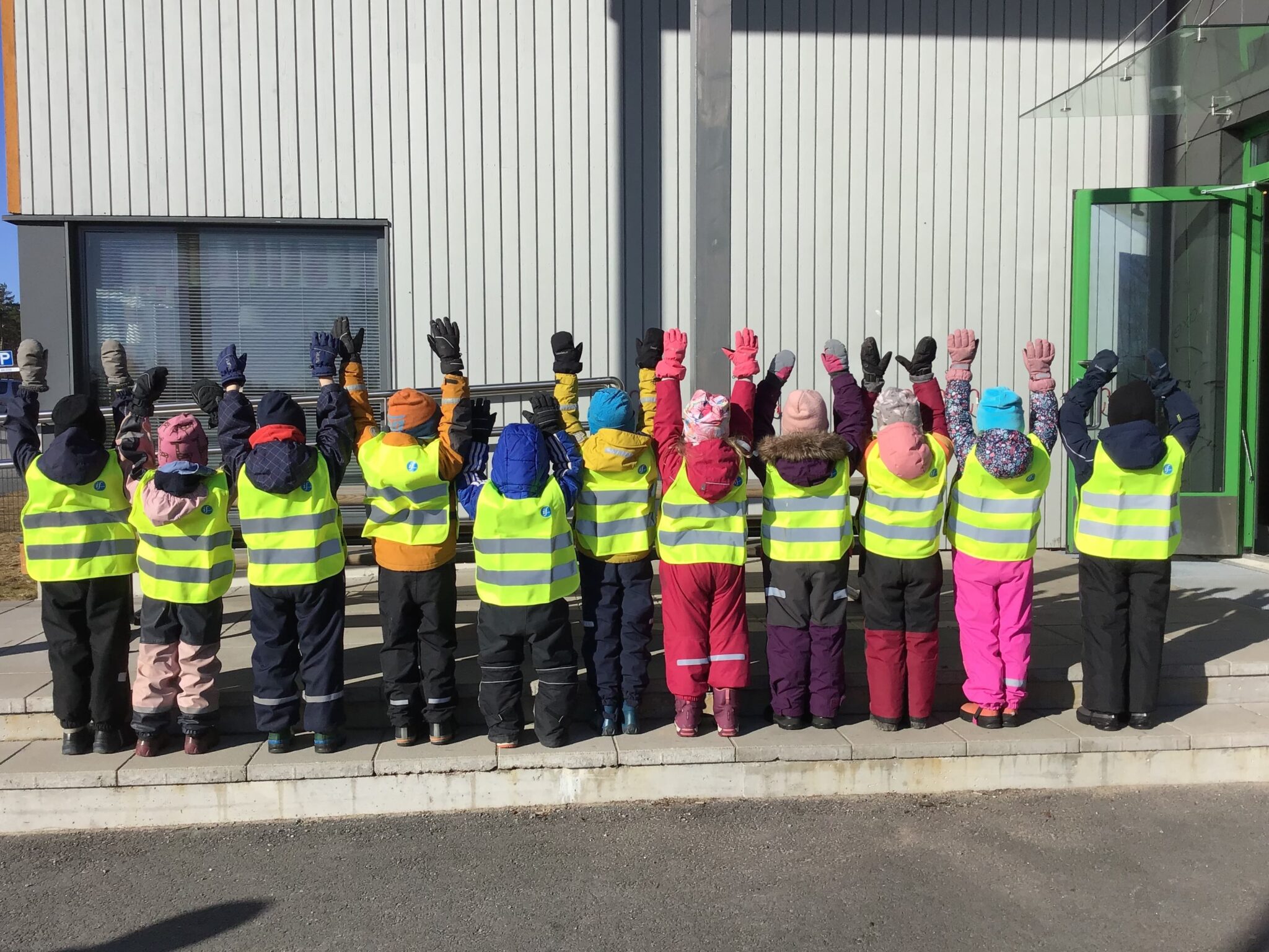 Barn med reflexvästar står vända med ryggen mot kameran och händerna sträckta i luften
